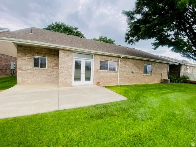 Brick ranch home with a spacious concrete patio, manicured lawn, and mature landscaping