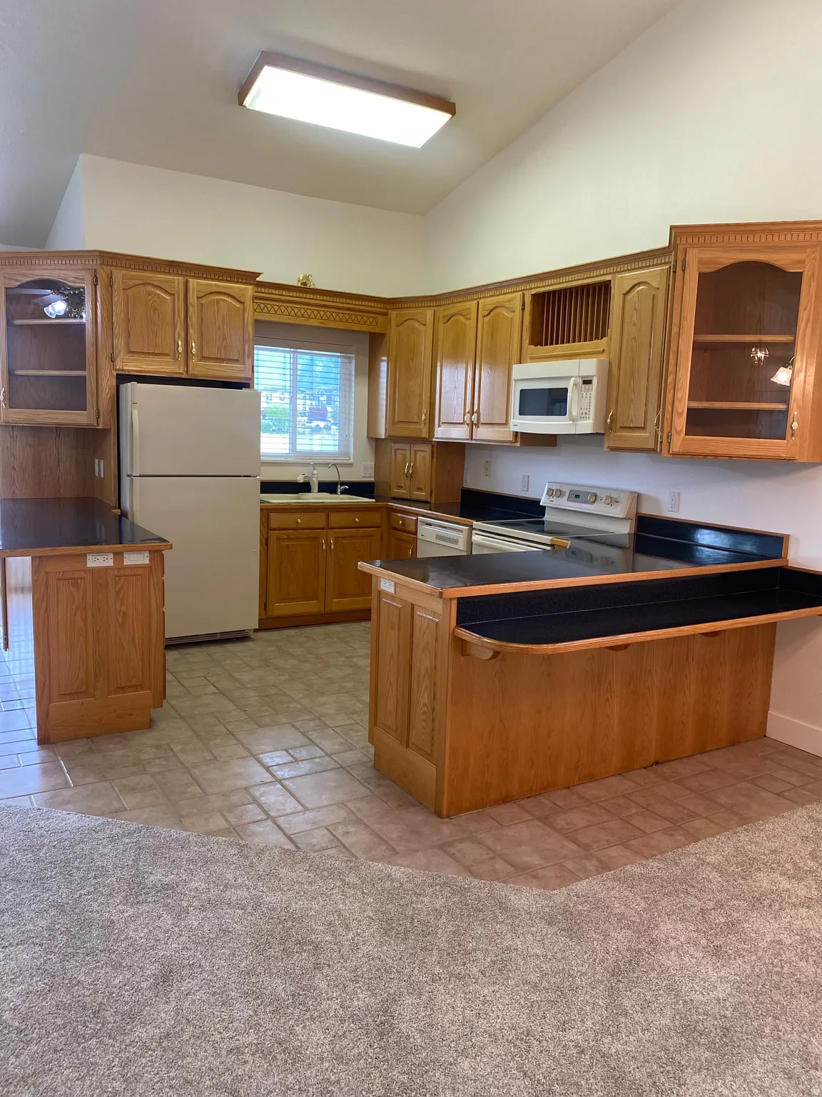 Kitchen featuring wood-finish cabinetry, dark countertops, white appliances, and a vaulted ceiling