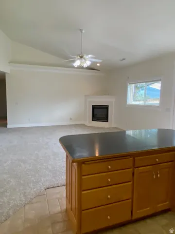 Vaulted ceiling, ceiling fan, corner fireplace, tiled flooring, and wood cabinetry with a dark countertop