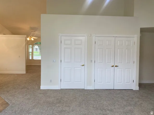 Vaulted ceiling with a ceiling fan, plush carpet flooring, paneled interior doors, and a window with an arched transom