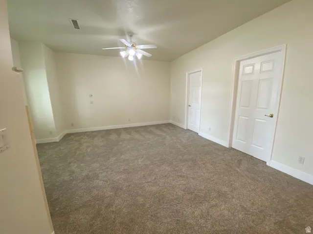 Spacious room featuring neutral carpet flooring, a ceiling fan with integrated lighting, and two panel doors