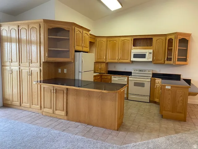 U-shaped kitchen featuring wood cabinetry, black countertops, integrated appliances, and a vaulted ceiling