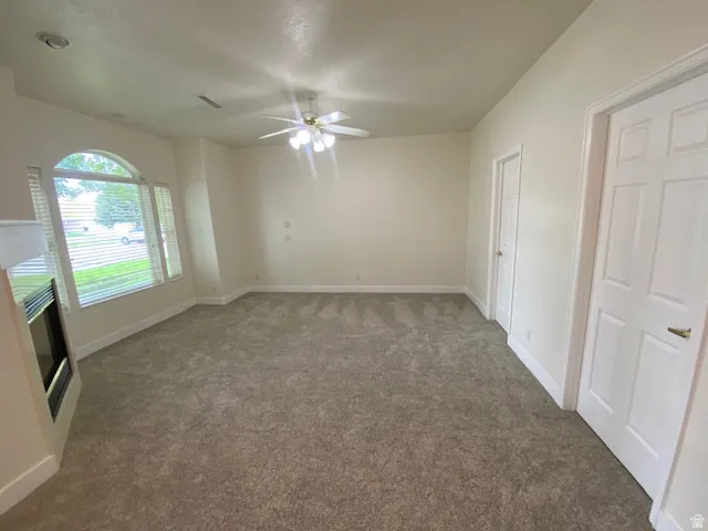 Spacious carpeted room featuring neutral tones, ceiling fan with integrated lighting, large arched window with plantation shutters, and dual six-panel closet doors providing abundant storage
