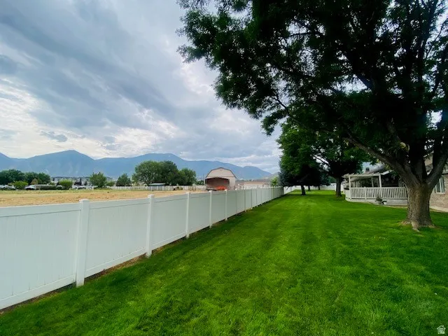 Expansive grounds featuring a meticulously manicured lawn, mature shade trees, and a white vinyl perimeter fence