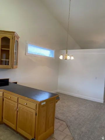 Vaulted ceiling with an overhead light fixture, wood cabinetry, dark countertops, and light gray carpeting