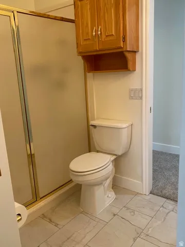 Ceramic tile flooring, white toilet, wood cabinetry, and a shower with frosted glass panels