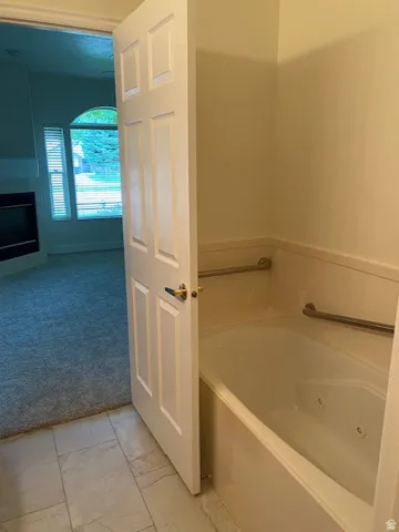 Master bathroom with soaking tub, dual grab bars, tile flooring, and direct access to the primary bedroom suite