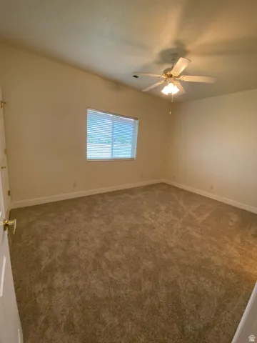 Carpeted room featuring a ceiling fan with integrated lighting and a window with blinds