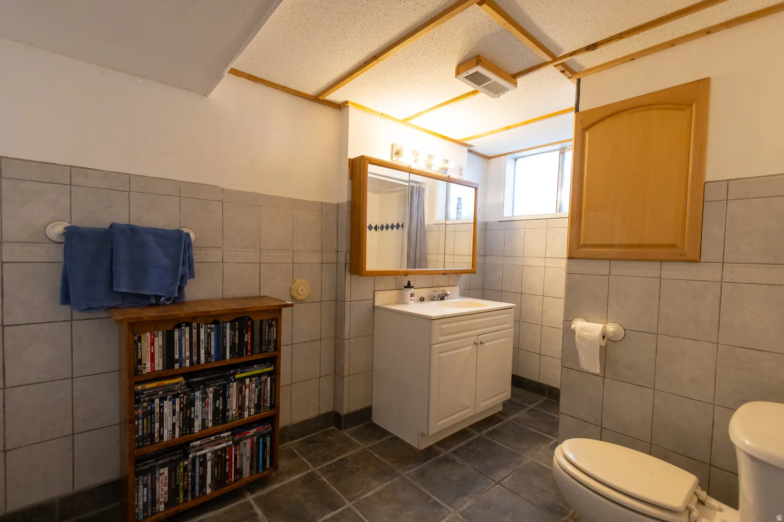 Full bathroom featuring light grey wall tiling, dark grey floor tiling, a white vanity with integrated sink, and a mirrored medicine cabinet with wood trim