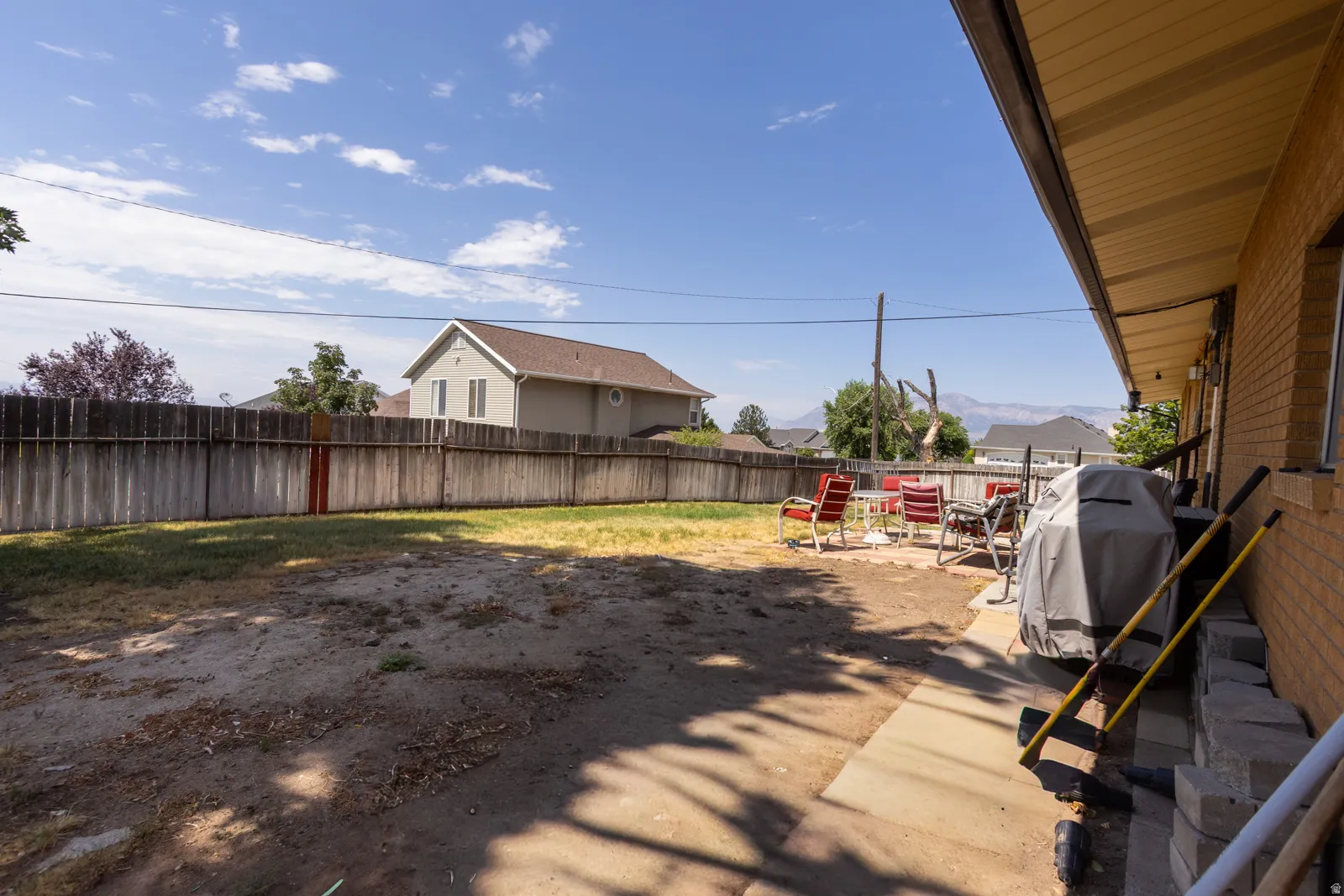 Expansive backyard featuring a wood privacy fence, concrete patio, and brick exterior