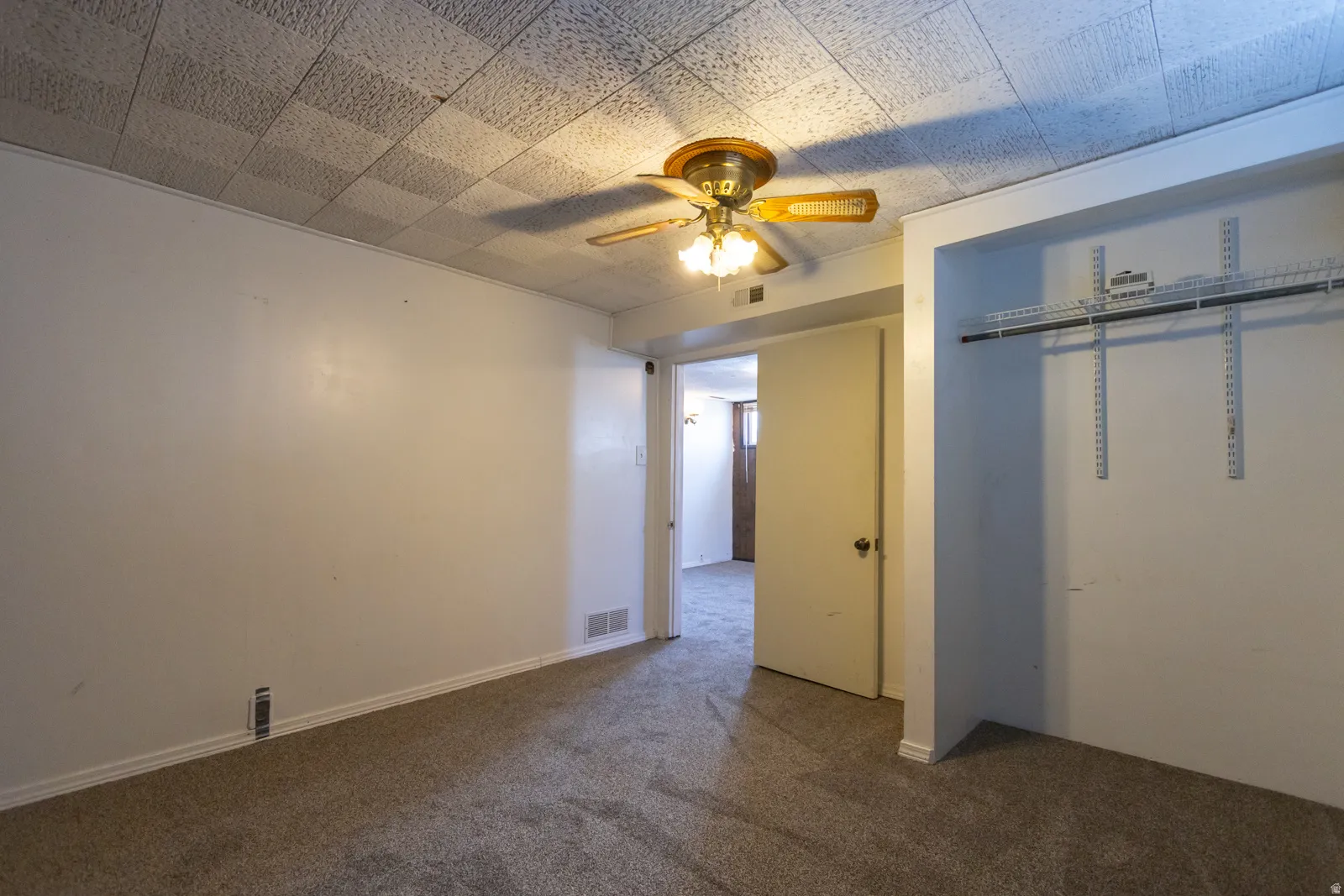 Carpeted room with white walls, a textured ceiling, a ceiling fan with light fixture, and an open closet featuring wire shelving