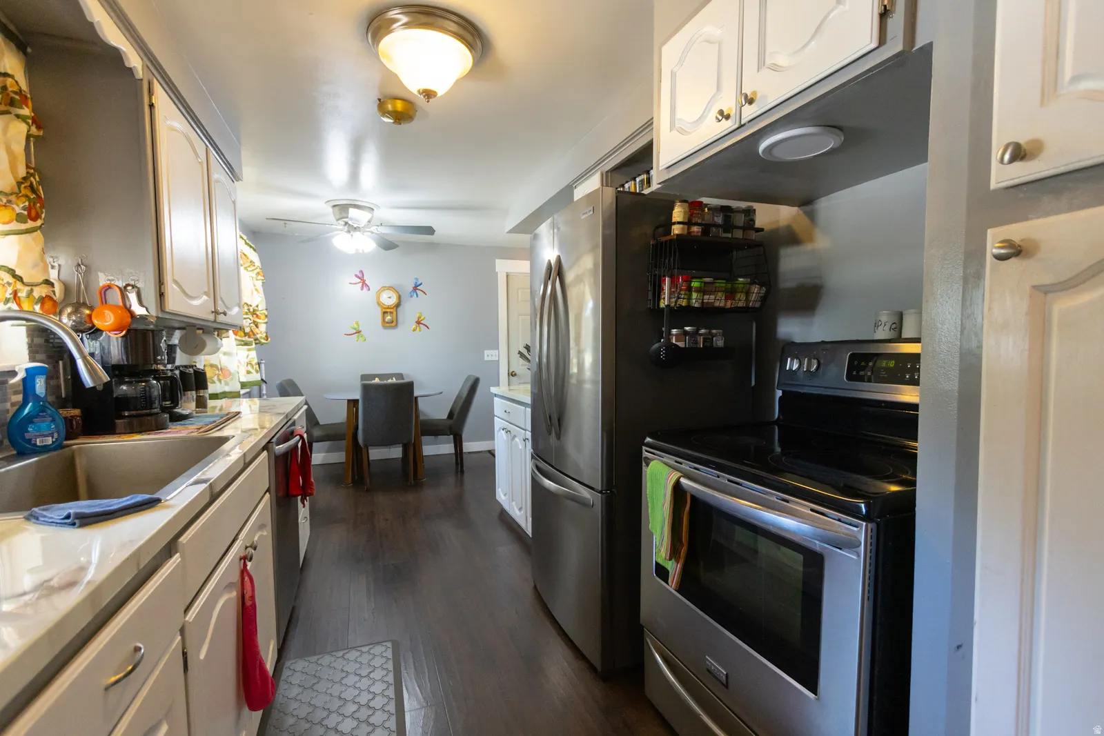 Kitchen featuring stainless steel appliances, light countertops, white cabinetry, dark wood-finish flooring, and a ceiling-mounted light fixture