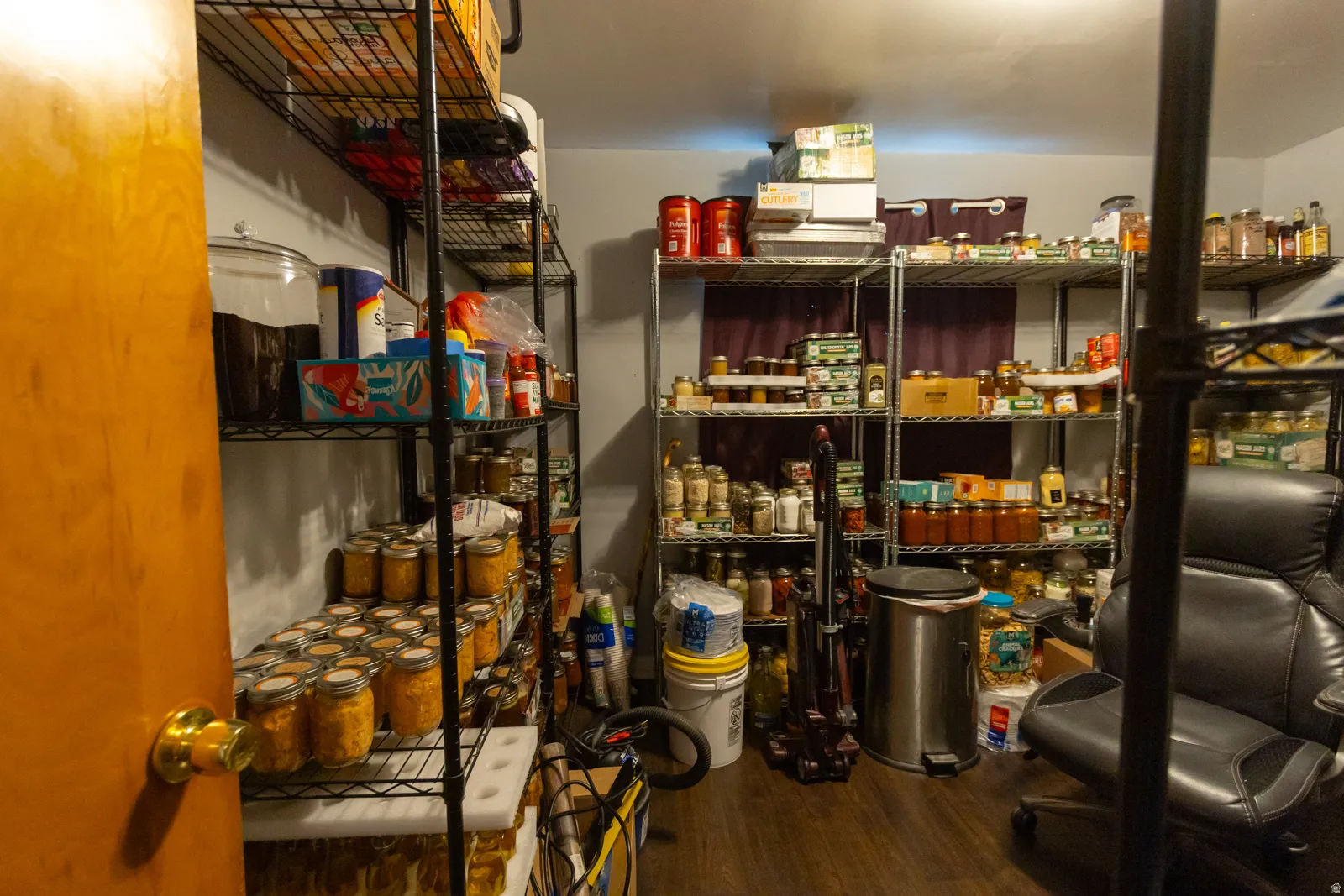 Dedicated storage room featuring multiple floor-to-ceiling metal shelving units, wood-finish flooring, and a neutral wall color