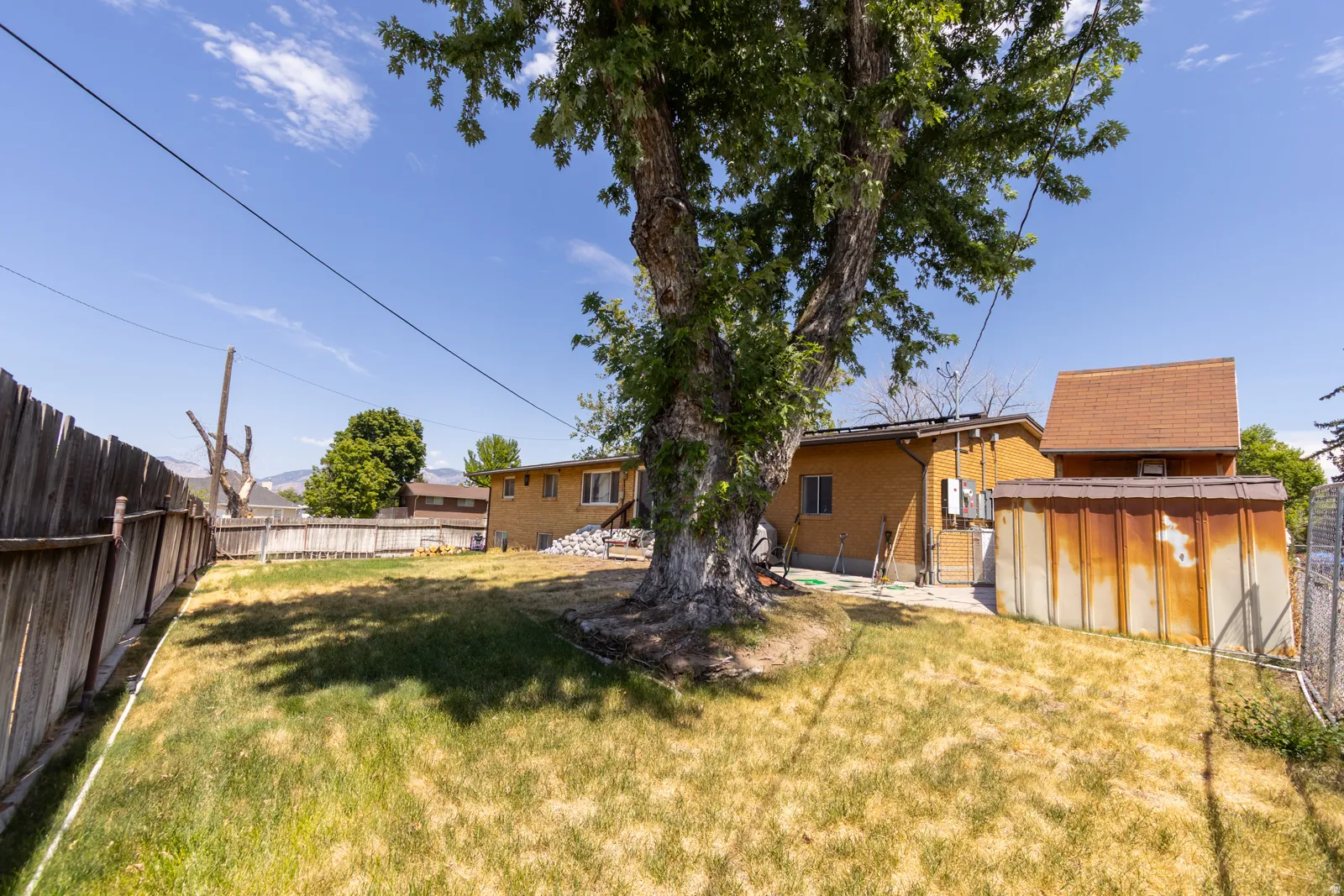Expansive backyard featuring a mature shade tree, full wood privacy fencing, and a brick-sided structure