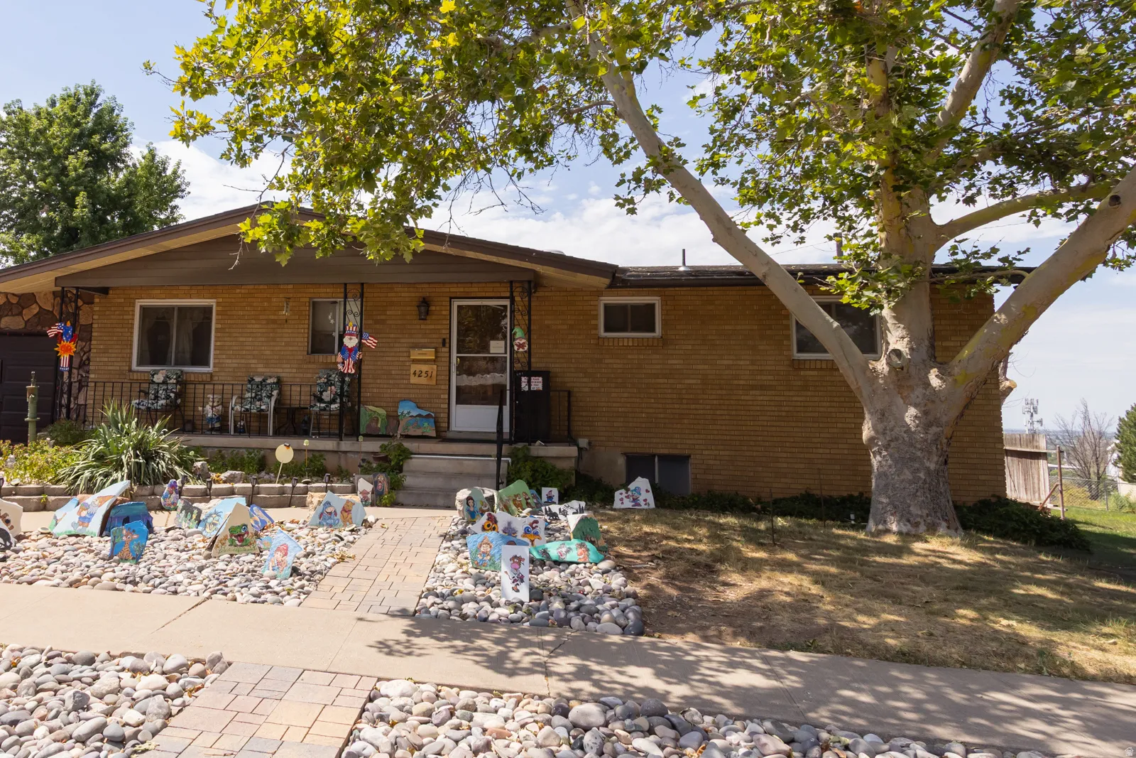 Brick and stone facade home featuring a covered front porch, mature shade tree, and a paver walkway with decorative rock landscaping