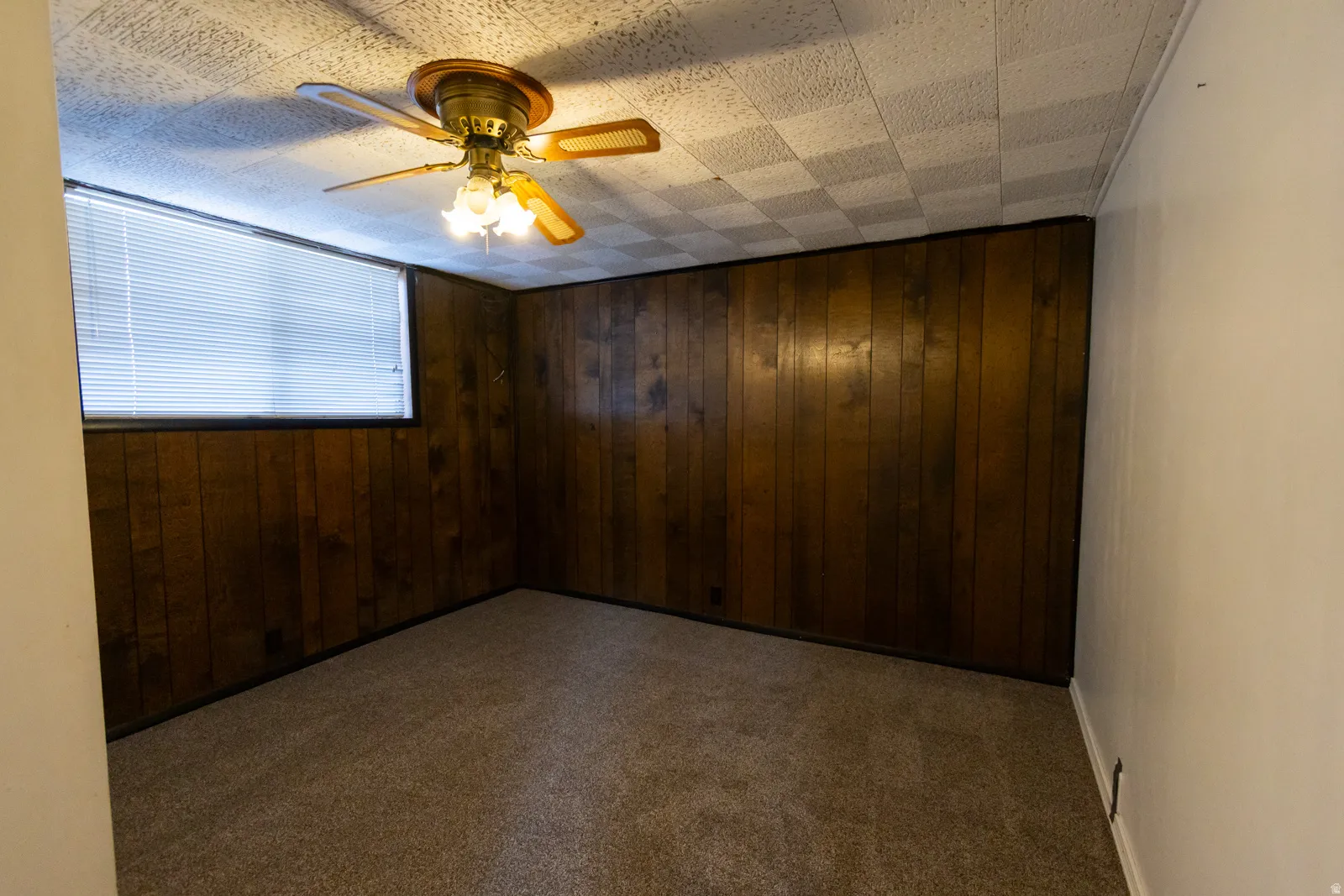 Room featuring wood-paneled walls, a drop ceiling, and carpeted flooring