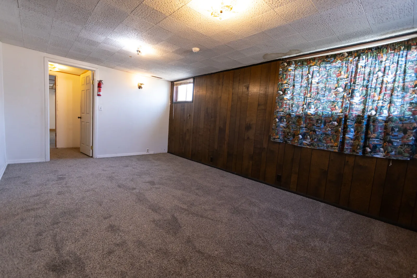 Spacious room featuring broadloom carpeting, a ceiling with acoustic tiles, and wood-paneled accent walls
