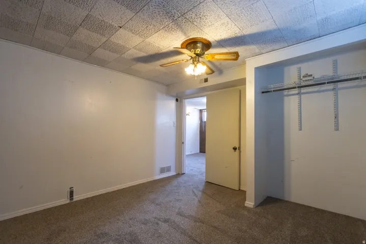Carpeted room with white walls, a textured ceiling, a ceiling fan with light fixture, and an open closet featuring wire shelving