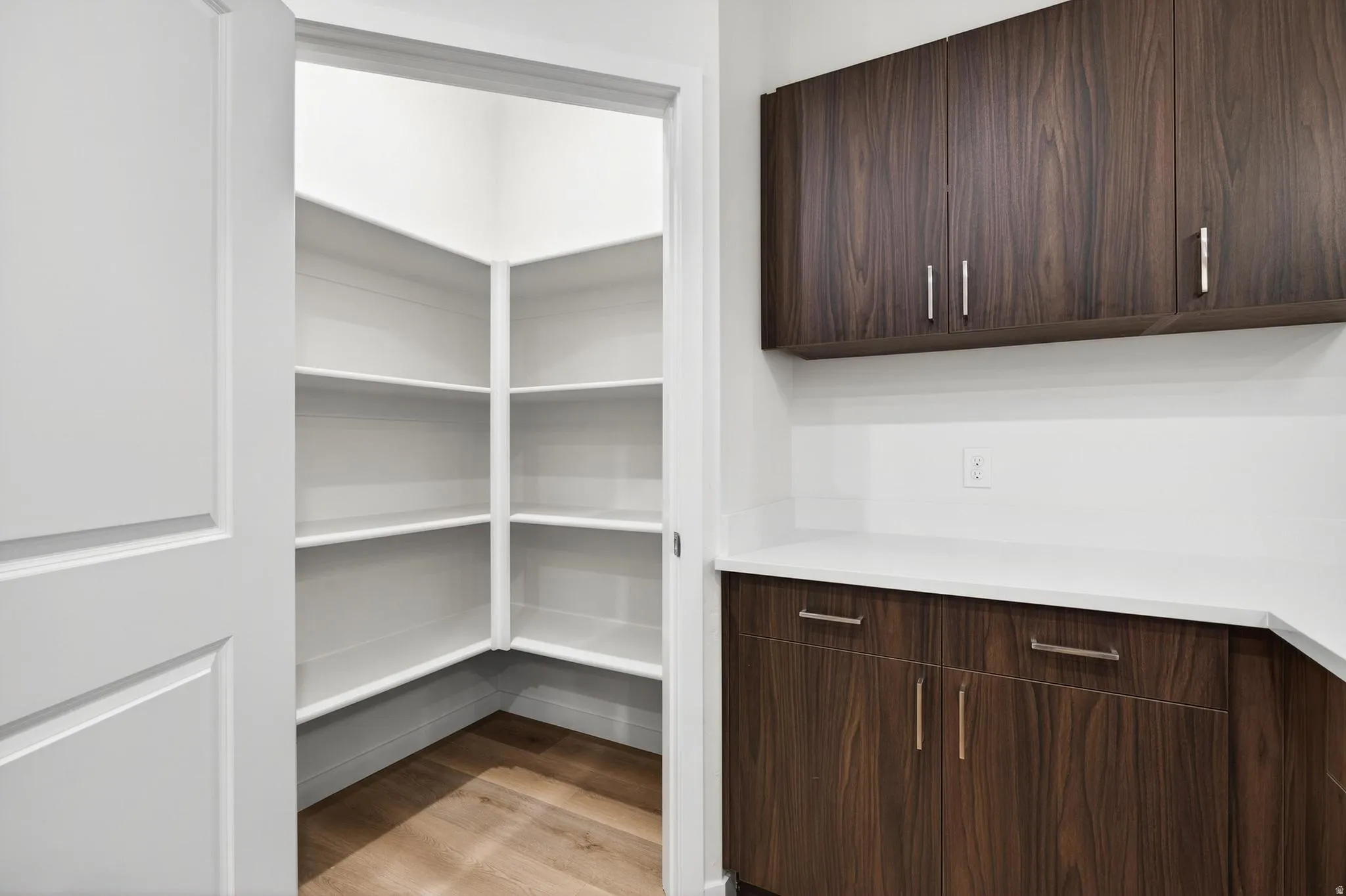 Walk-in pantry with extensive white shelving and wood-finish flooring