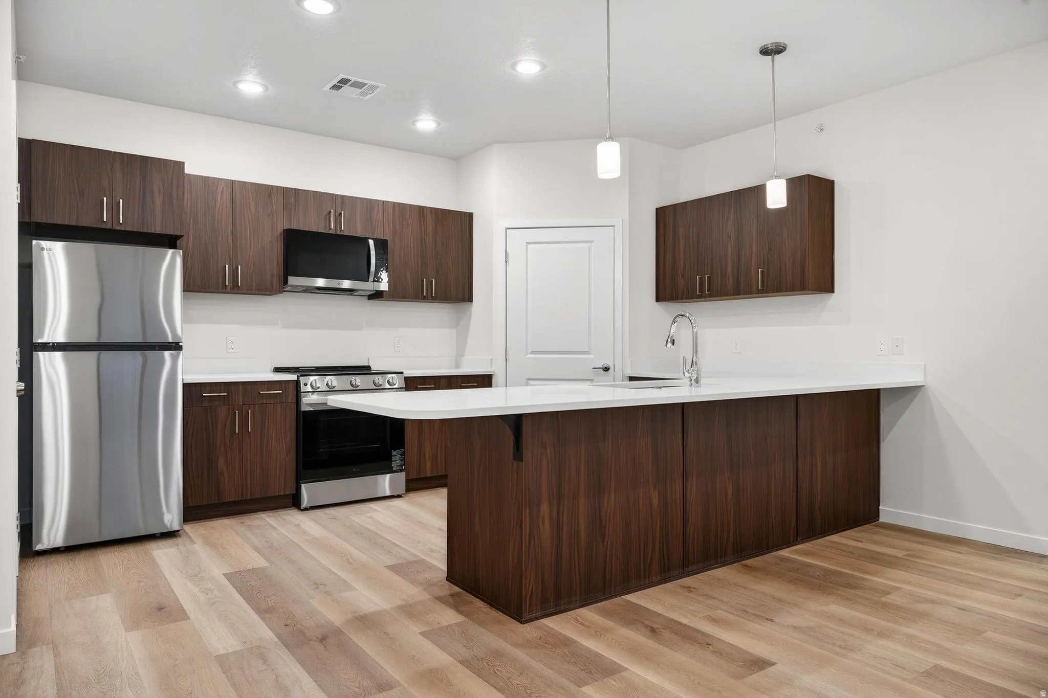 Contemporary kitchen featuring wood-finish cabinetry, stainless steel appliances, and light-toned countertops