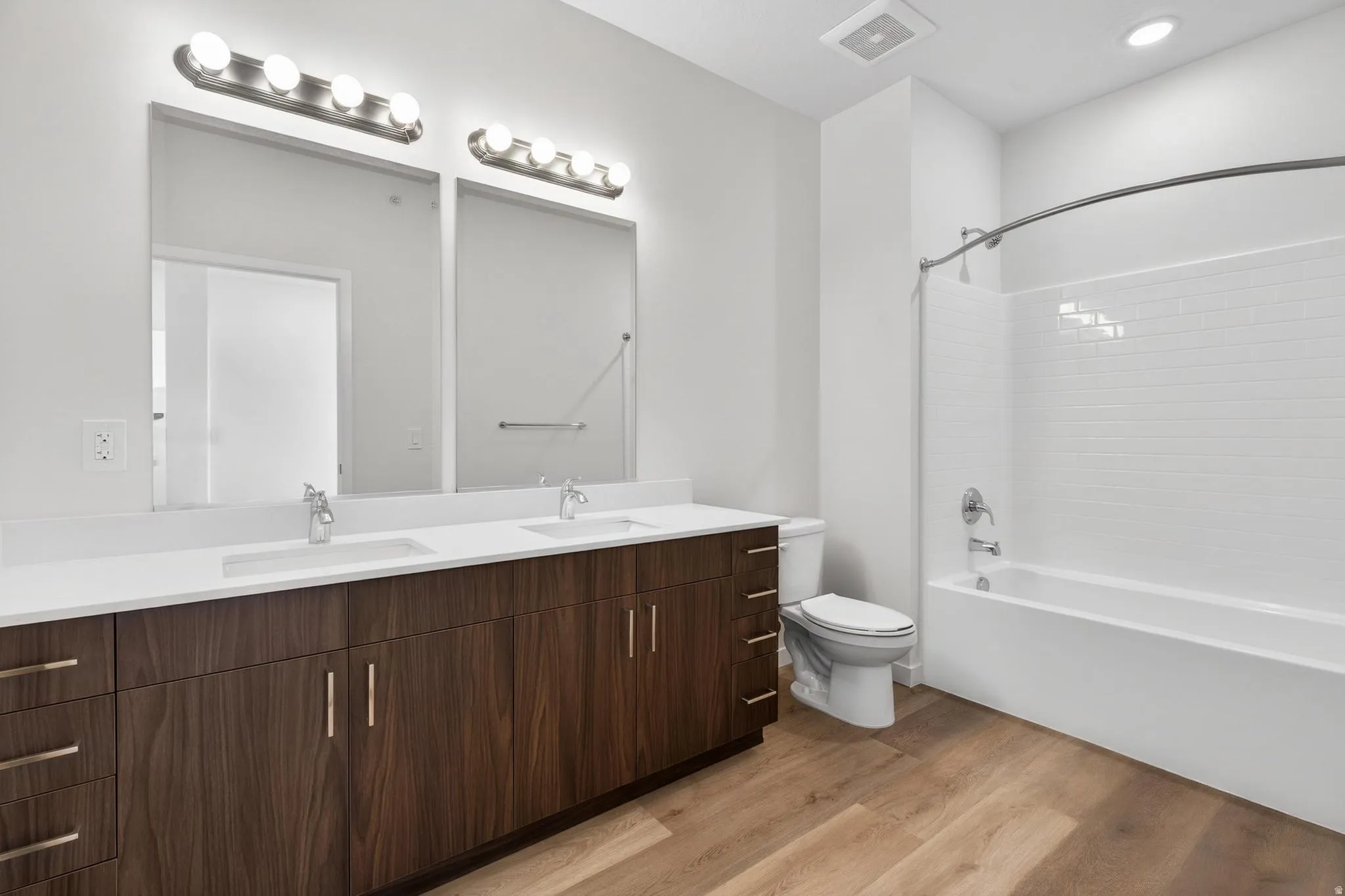 Spacious bathroom featuring a double vanity with wood-finish cabinetry and white countertops, dual rectangular sinks, and an integrated tub-shower combination with white subway tile surround