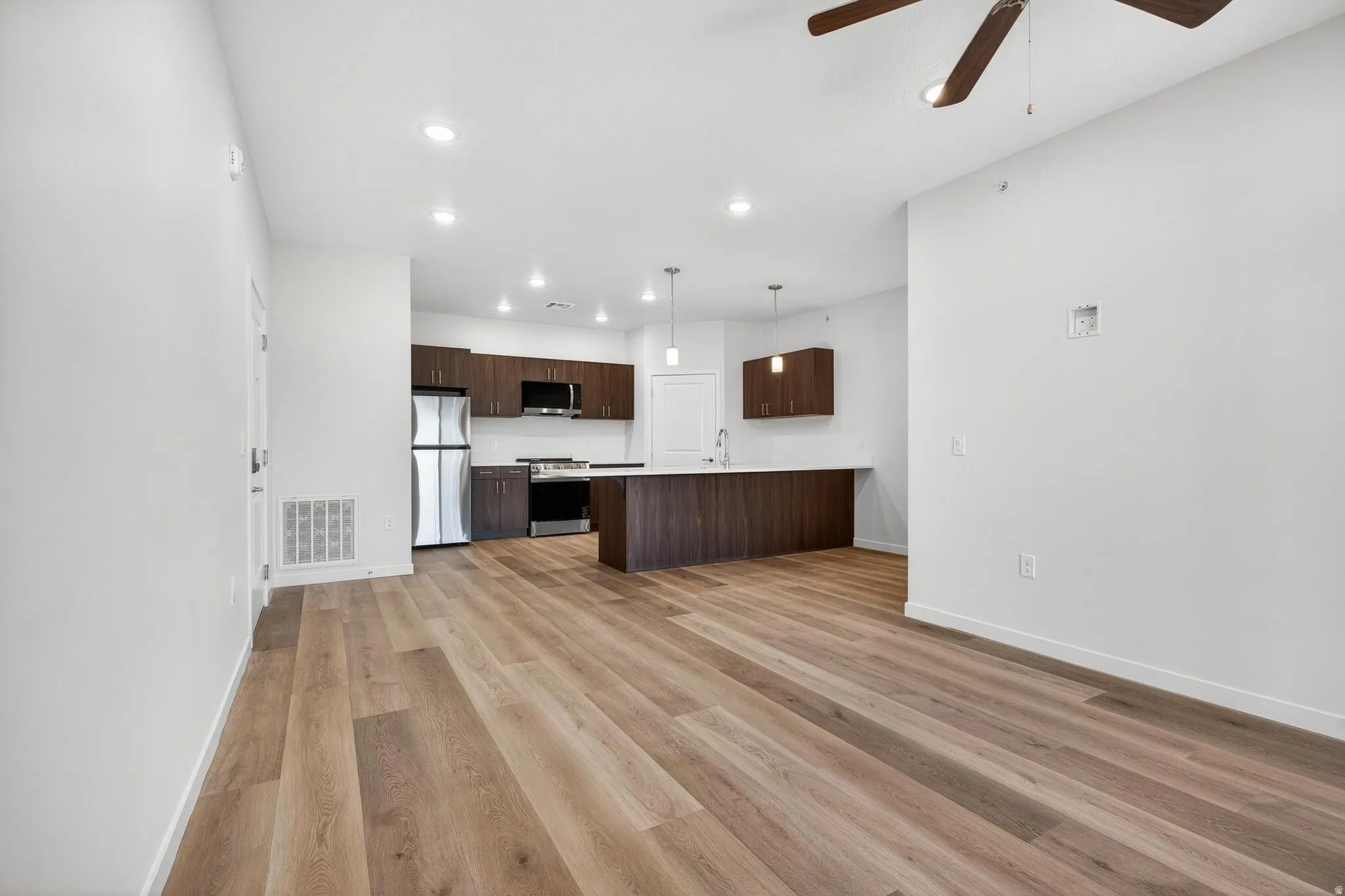 Open-concept living area with wood-finish flooring, a contemporary ceiling fan, and recessed lighting