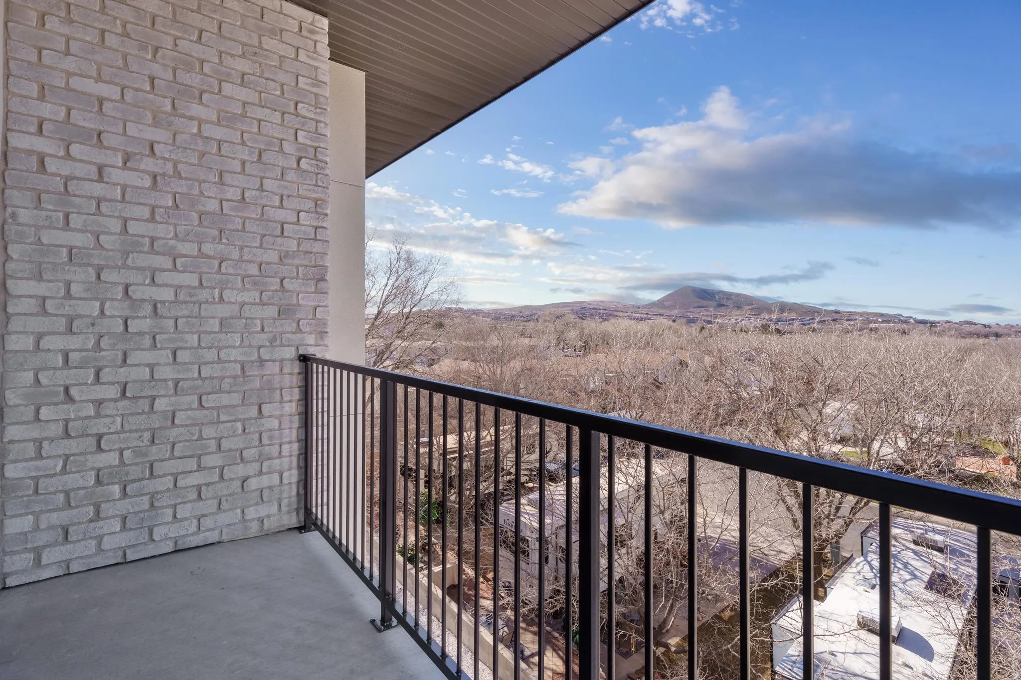 Balcony featuring a concrete floor, light gray brick wall, and black metal railing