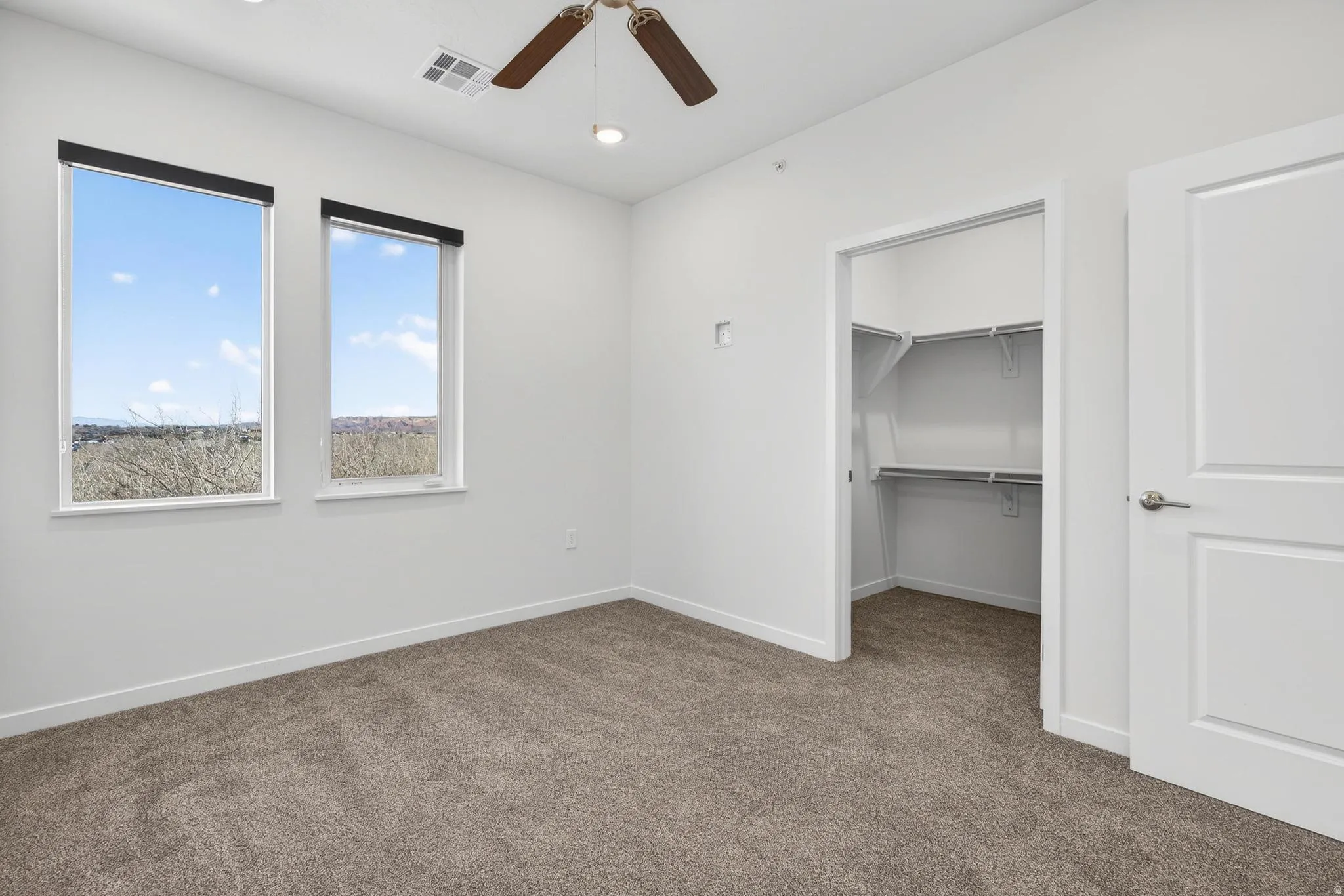 Bright room featuring two windows with roller shades, a ceiling fan, recessed lighting, and a walk-in closet with shelving