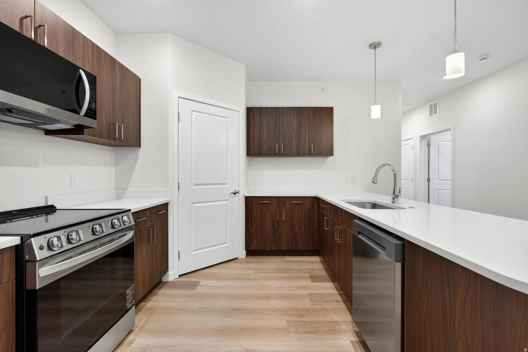 Modern kitchen featuring wood-finish cabinetry, white countertops, stainless steel appliances, and wood-look flooring