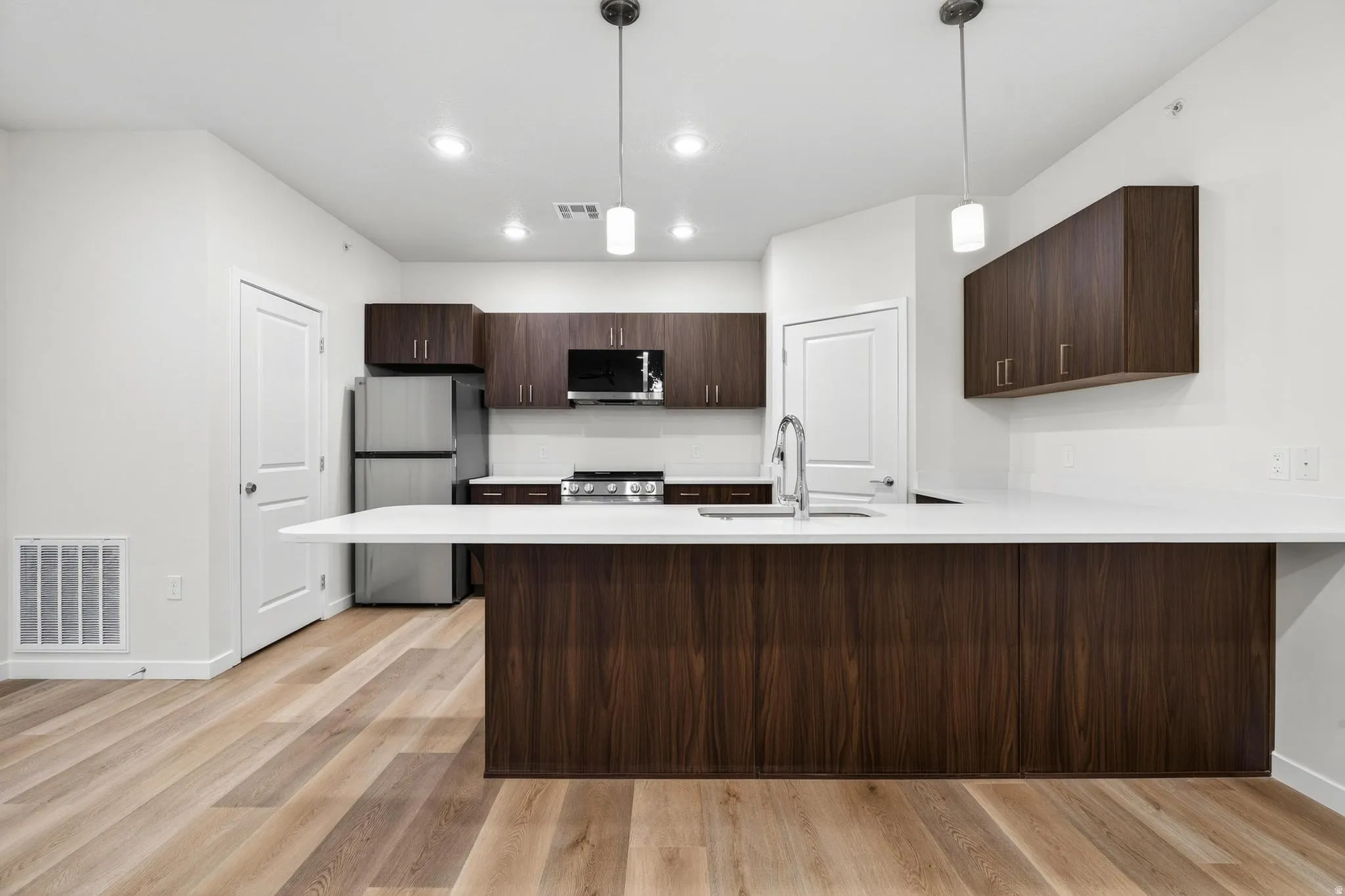 Modern kitchen featuring a large island with an integrated sink, stainless steel appliances, wood-finish cabinetry, recessed lighting, and pendant fixtures