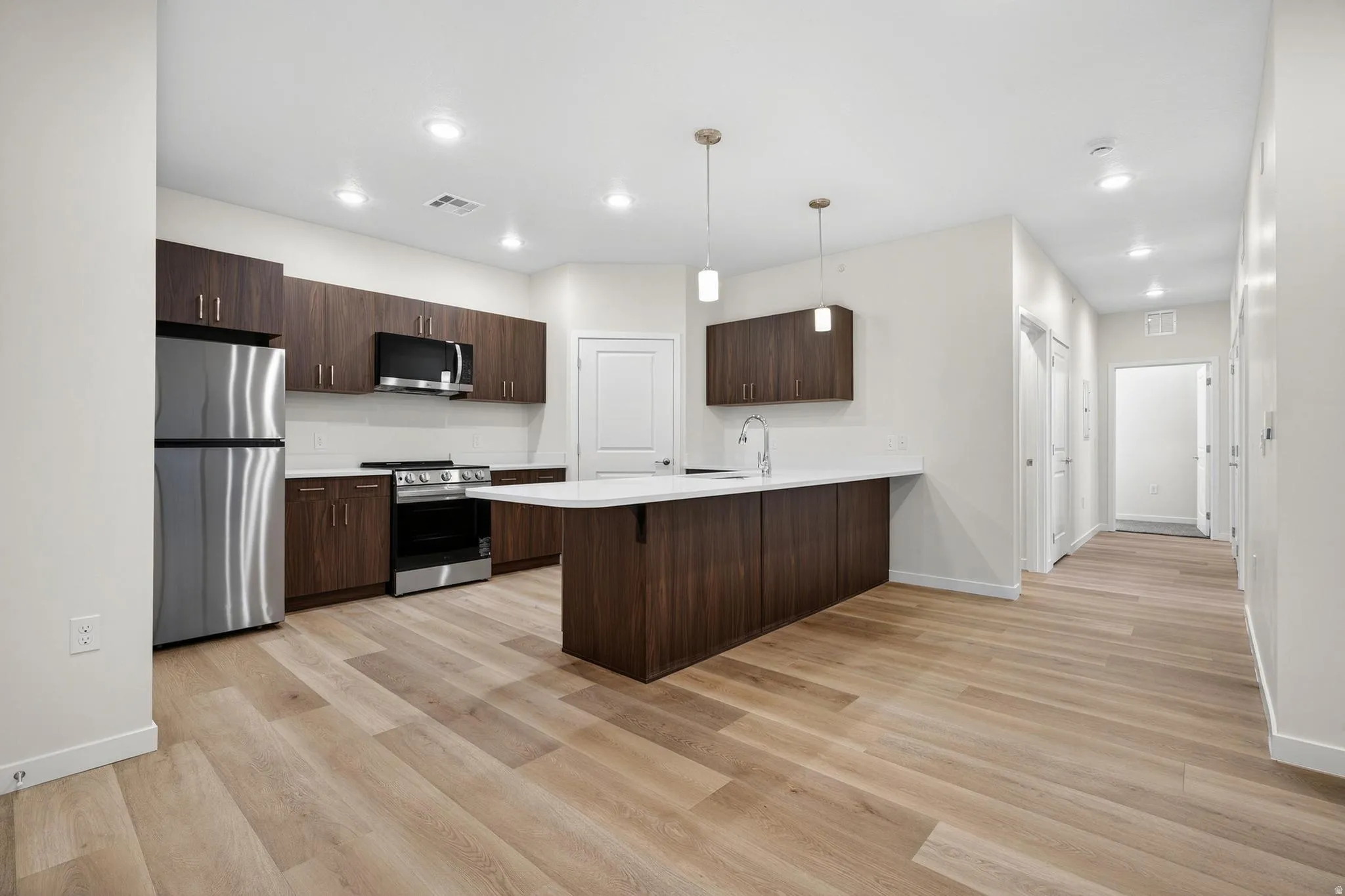 Open-concept kitchen featuring wood-finish flooring, dark wood cabinetry, white countertops, and stainless steel appliances