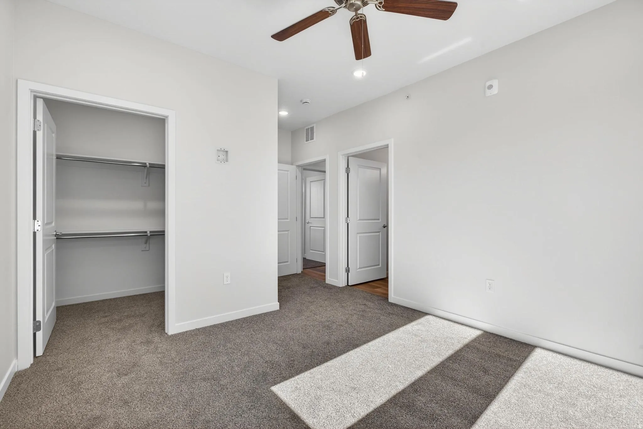 Carpeted interior space featuring a ceiling fan with wood-finish blades, a white paneled door, and a closet with shelving and hanging rods