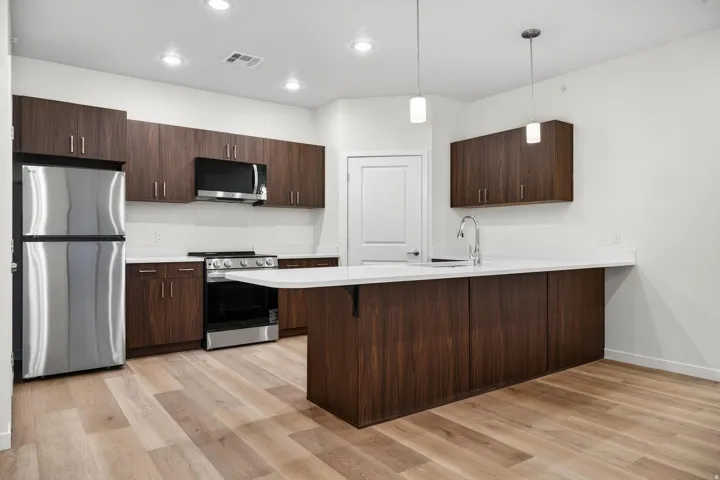 Contemporary kitchen featuring wood-finish cabinetry, stainless steel appliances, and light-toned countertops