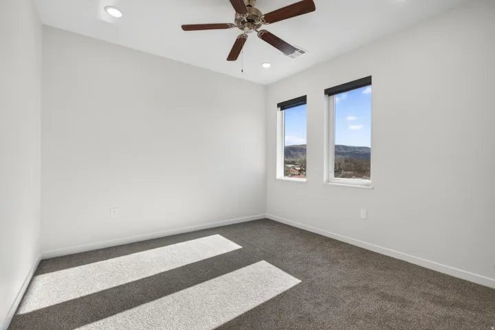 Bright room featuring two windows with roller shades, a ceiling fan, recessed lighting, and grey carpet flooring