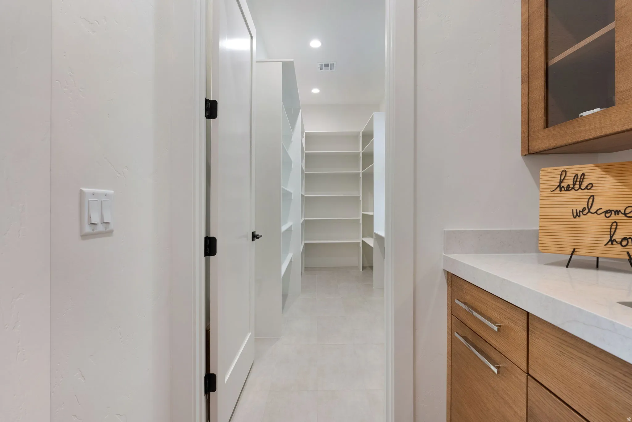 Spacious walk-in pantry featuring built-in shelving, recessed lighting, and light-toned flooring