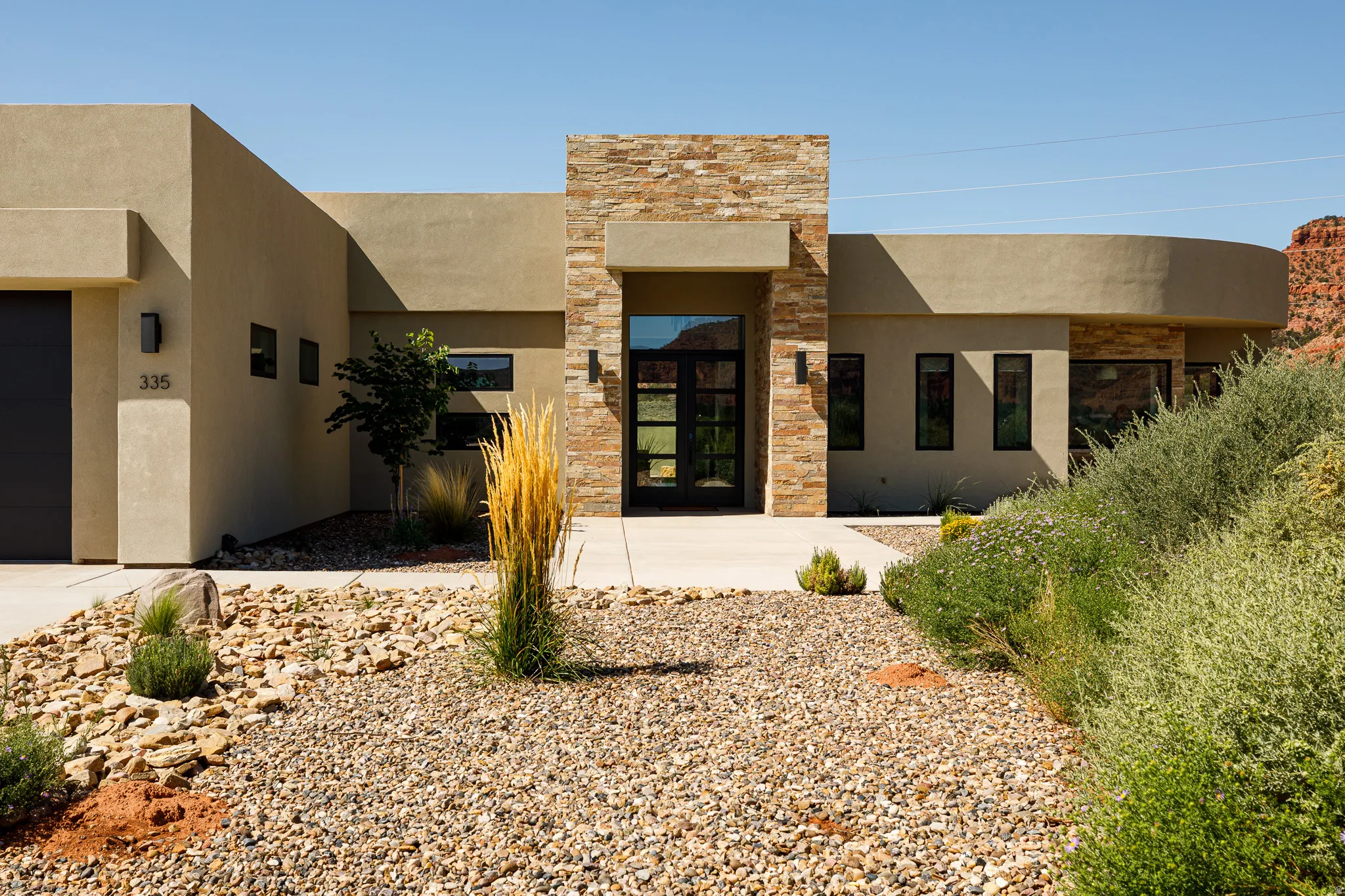 Modern exterior architecture featuring stucco and stacked stone accents, a full-lite entry door, and integrated wall sconces