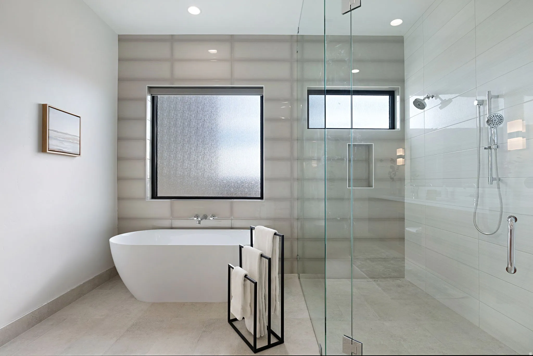 Modern bathroom featuring a freestanding soaking tub, a spacious glass-enclosed shower with dual shower heads, and large format floor tiling