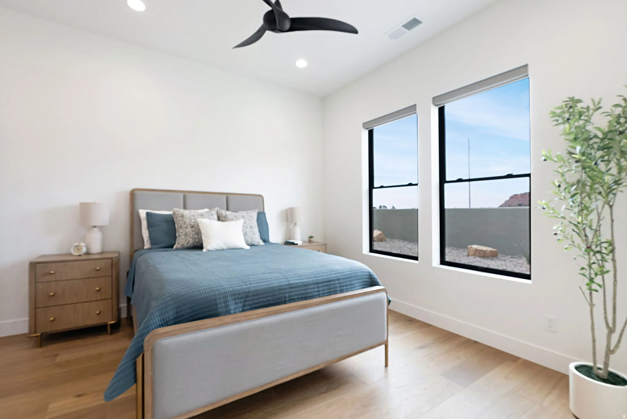 Spacious room featuring wood-finish flooring, two large windows with roller shades, a black ceiling fan, and recessed lighting