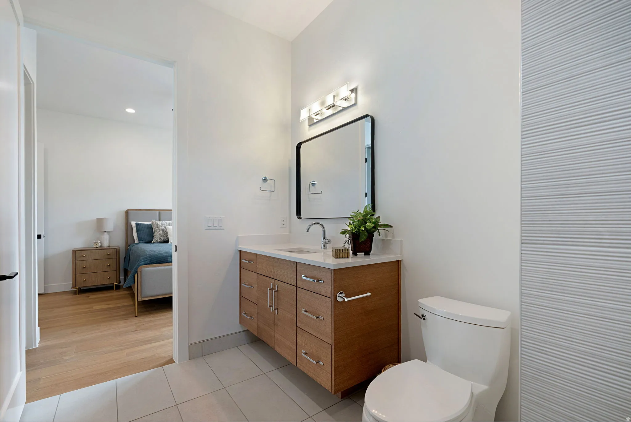 Modern bathroom featuring a wood-finish vanity with a light-toned countertop, a rectangular mirror with a black frame, and a wall-mounted light fixture