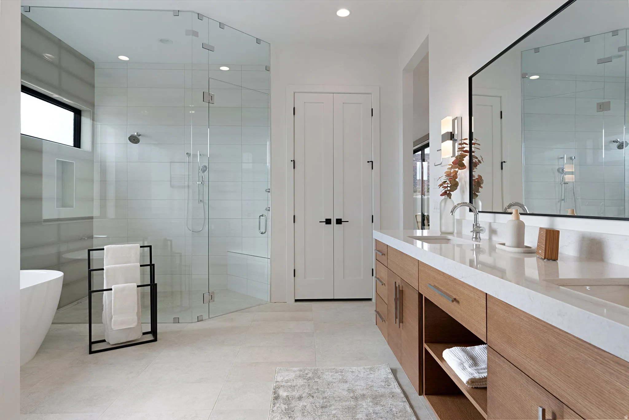 Modern bathroom featuring a frameless glass shower enclosure with a built-in bench, a freestanding soaking tub, and a dual-sink vanity with wood-finish cabinetry and light-colored countertops