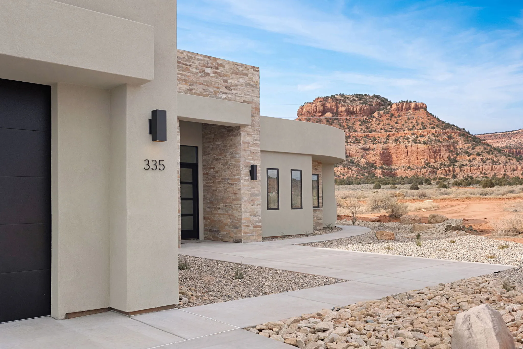 Modern stucco and stone exterior featuring a black garage door and exterior lighting