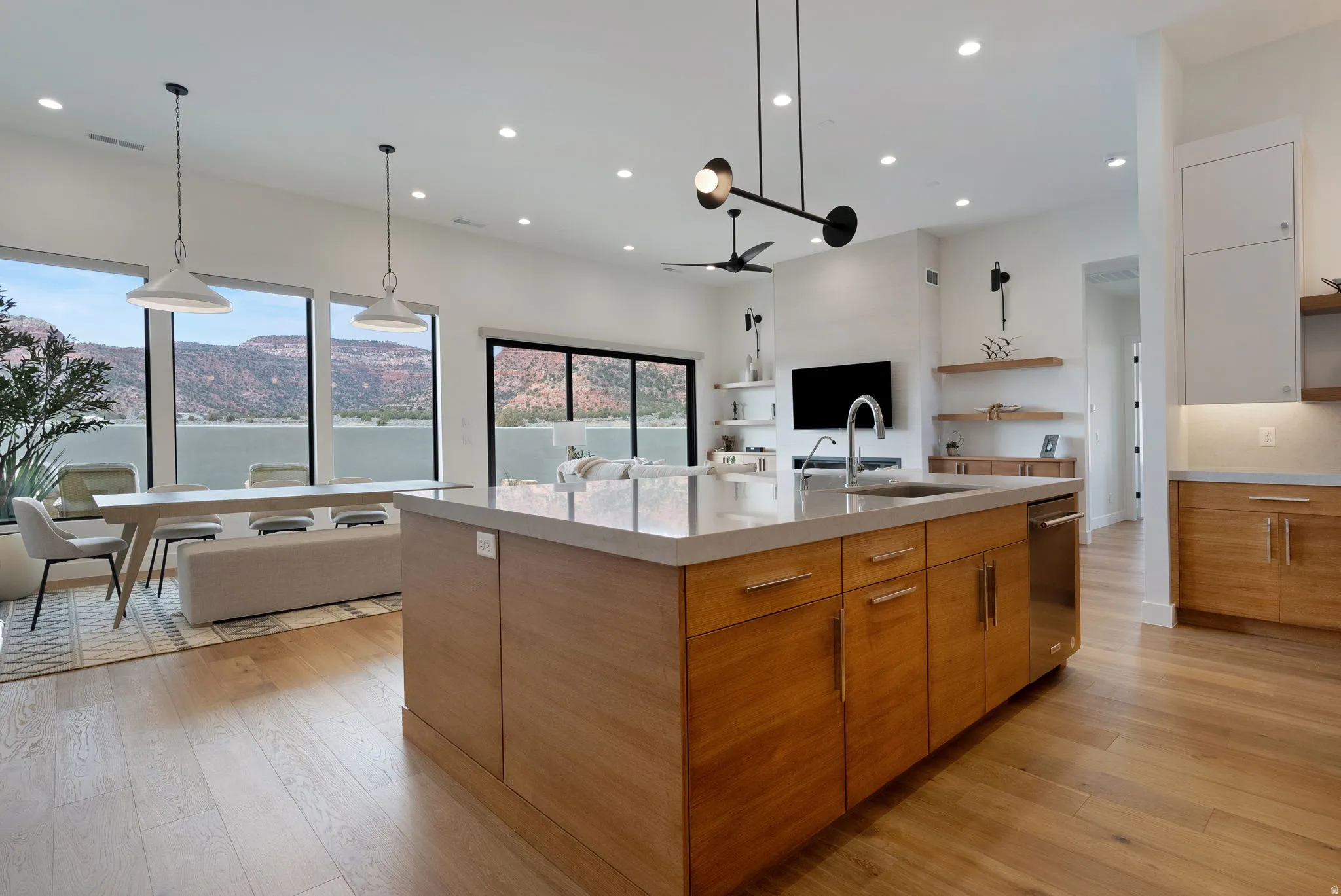 Open-concept living space featuring wood-finish flooring, a kitchen island with integrated sink, and floor-to-ceiling windows with mountain scenery
