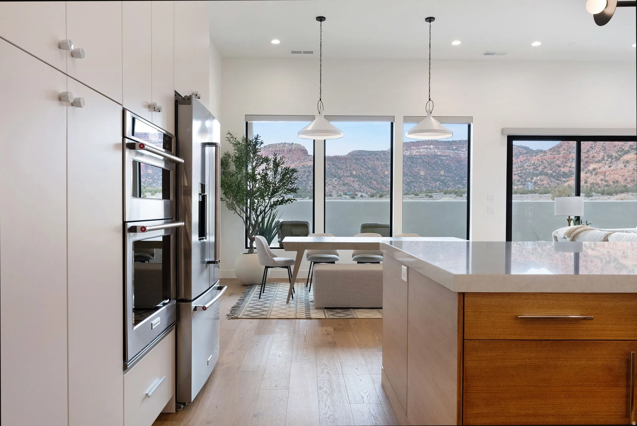 Modern kitchen featuring a spacious island with a light-toned countertop, integrated stainless steel appliances, extensive white cabinetry, and wood-finish flooring