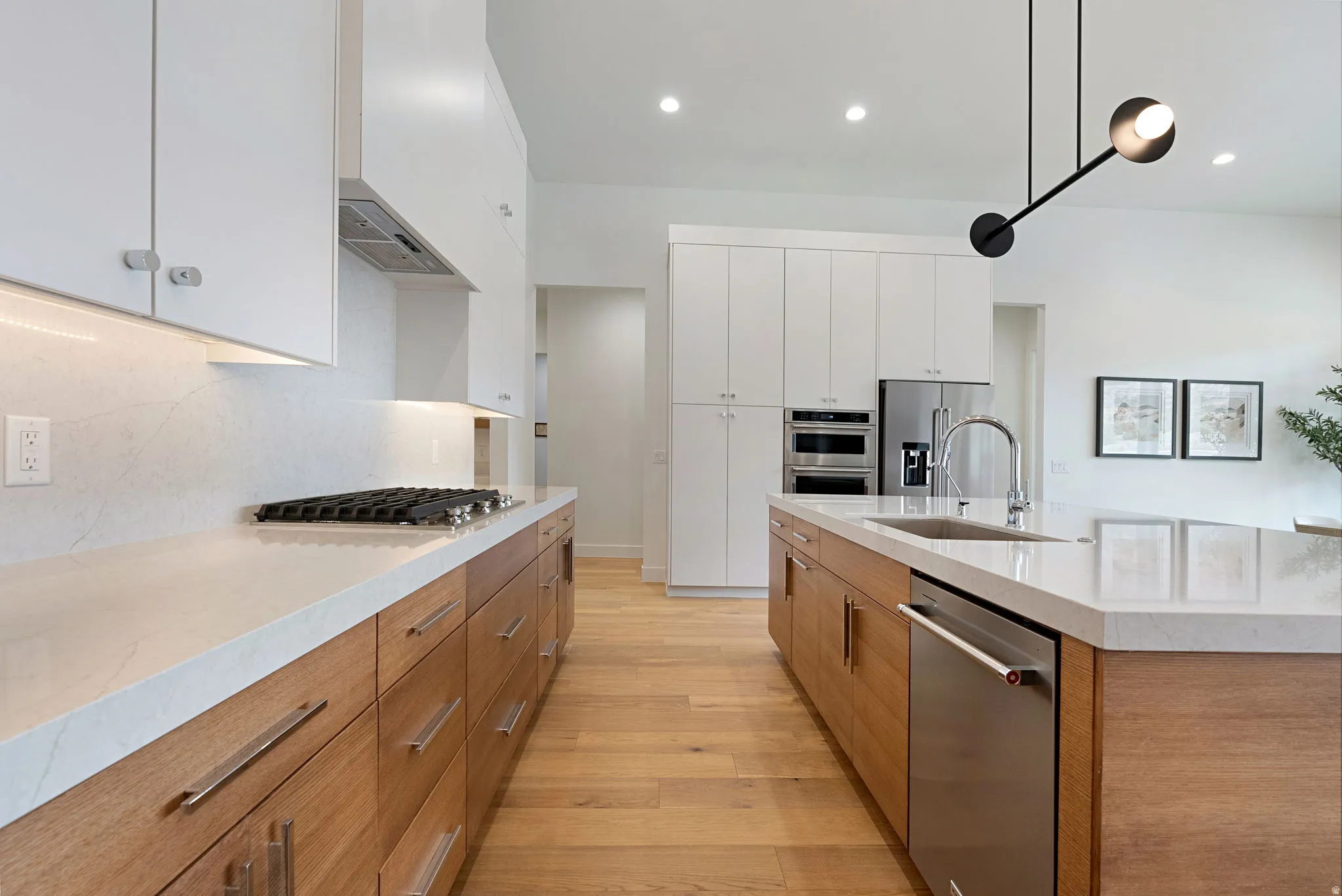 Contemporary kitchen featuring two-tone cabinetry, light wood-finish flooring, and a central island with an undermount sink