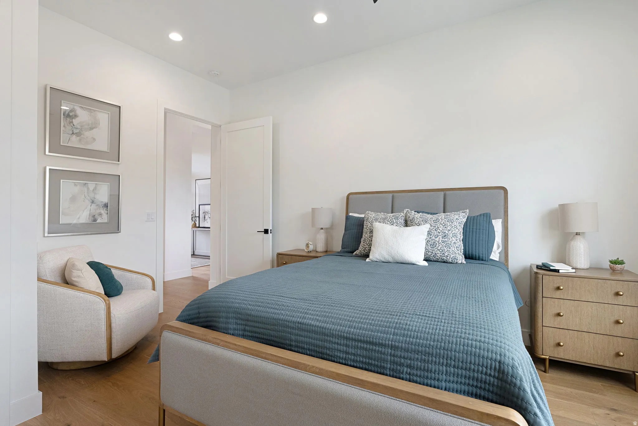 Recessed lighting illuminates this bright room featuring wood-finish flooring, a solid-core door with matte black hardware, and crisp white walls