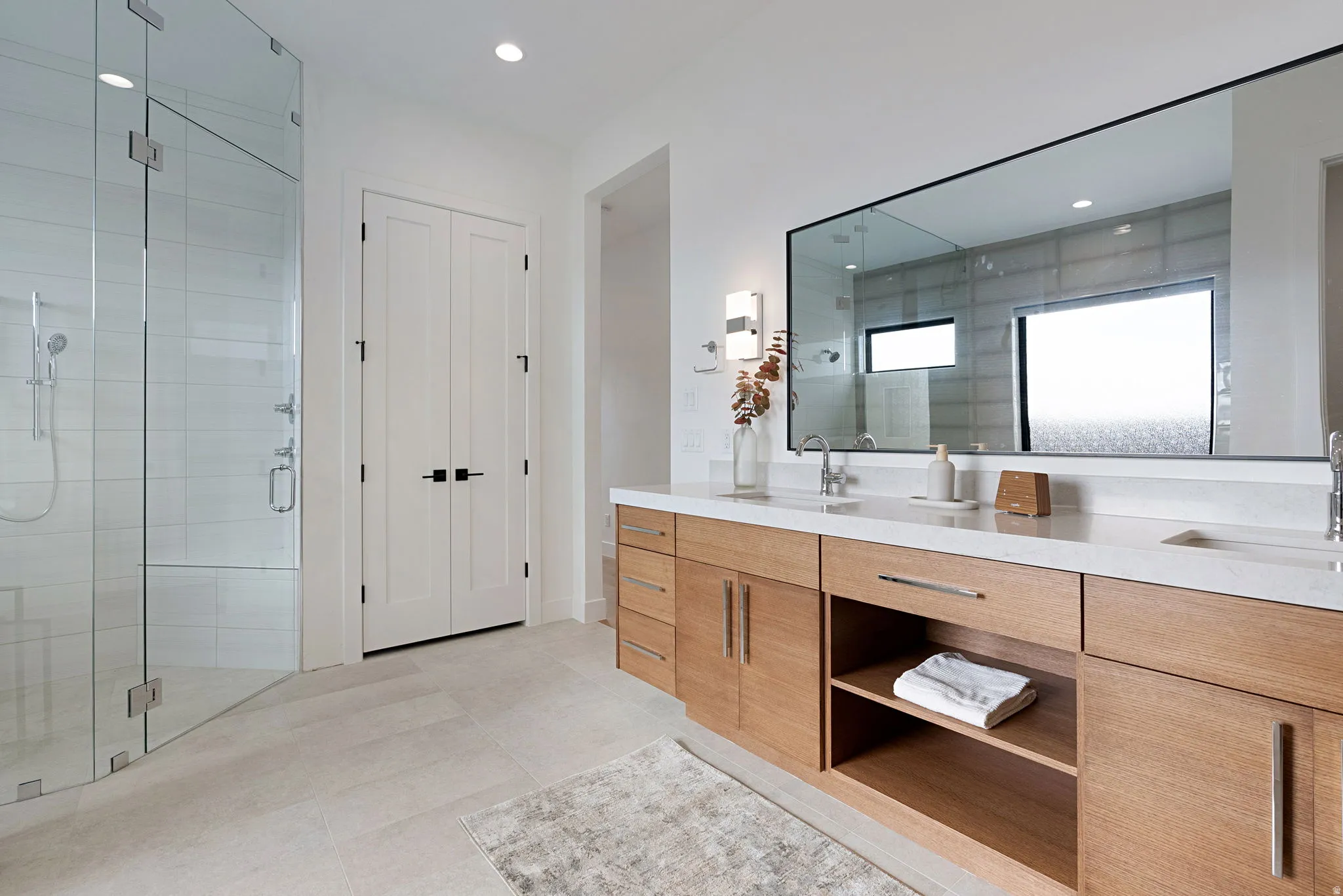 Contemporary bathroom featuring a spacious glass-enclosed shower, a double vanity with wood-finish cabinetry, light-toned countertops, a large rectangular mirror, and recessed lighting