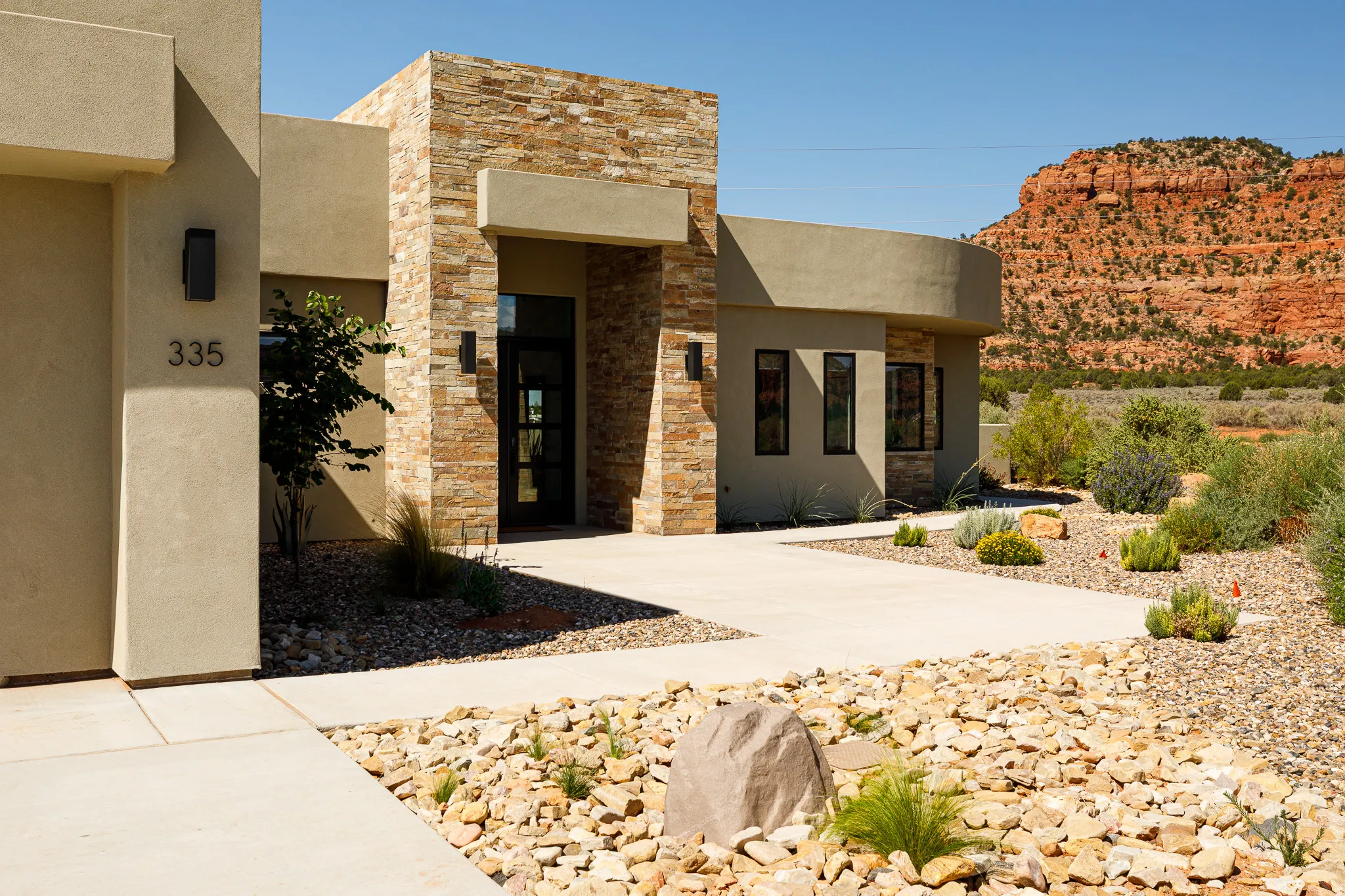 Stucco exterior with stacked stone accents, desert landscaping, and a concrete pathway leading to the entry