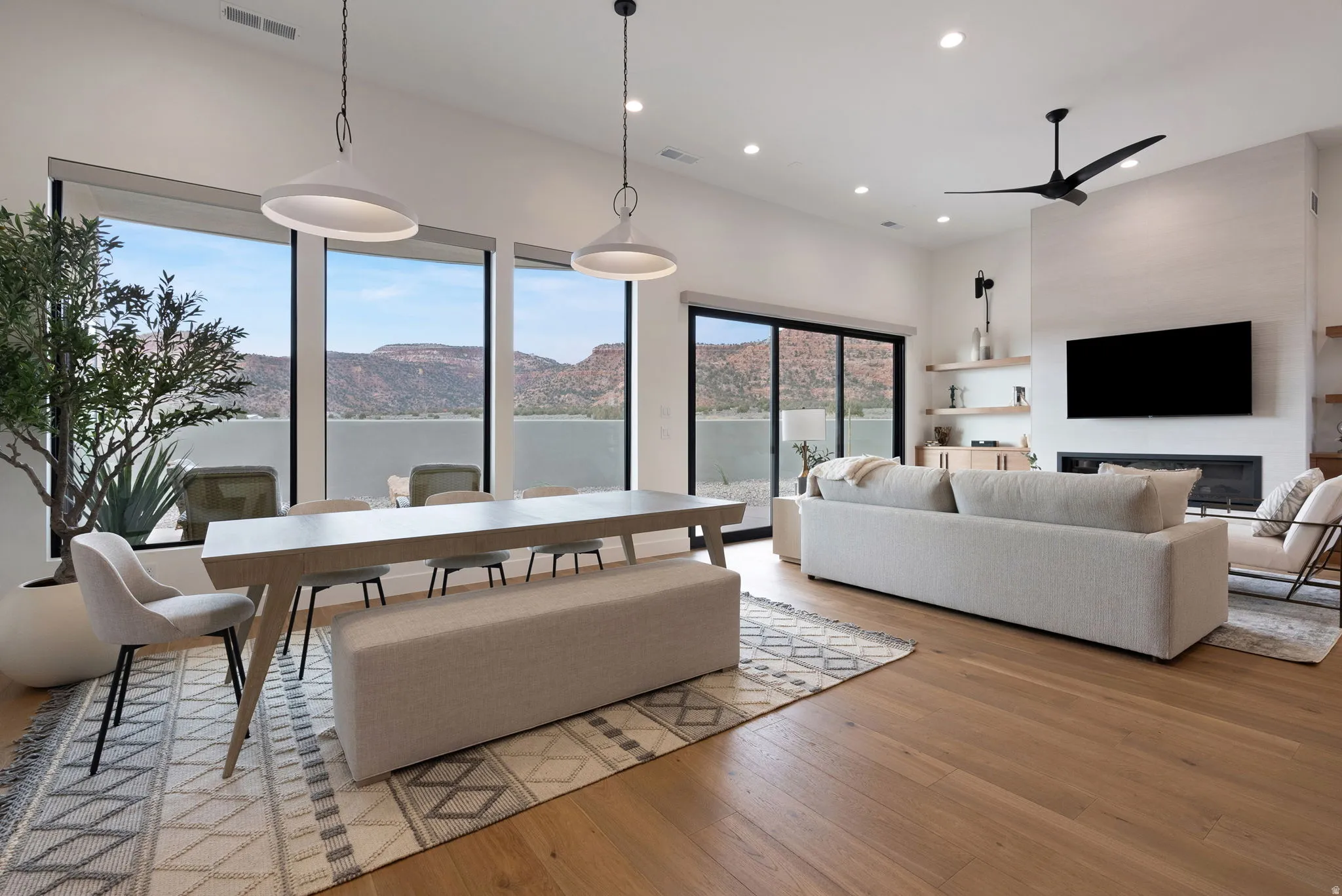 Open-concept living space featuring high ceilings, wood-finish flooring, a modern linear fireplace, recessed lighting, and expansive windows