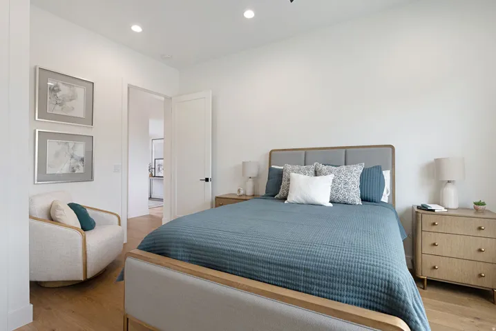Recessed lighting illuminates this bright room featuring wood-finish flooring, a solid-core door with matte black hardware, and crisp white walls