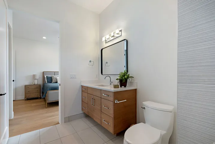 Modern bathroom featuring a wood-finish vanity with a light-toned countertop, a rectangular mirror with a black frame, and a wall-mounted light fixture